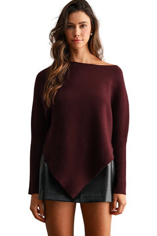 A woman modeling a dark burgundy off-the-shoulder knit sweater with a long asymmetrical draped hem, paired with a dark gray mini skirt, against a textured beige studio backdrop.