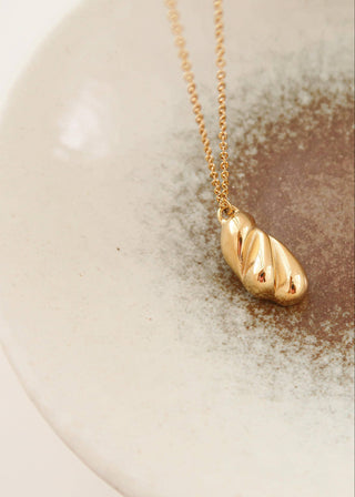 Gold necklace with a unique pendant on a ceramic plate