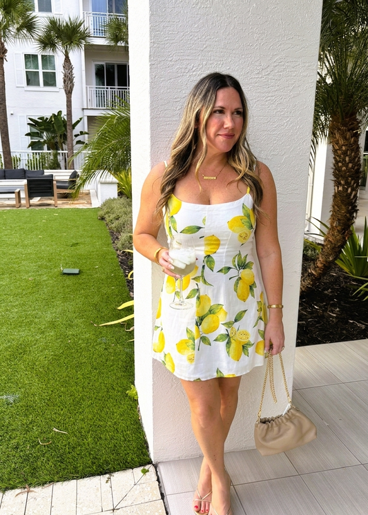 Woman in a white dress with yellow lemon pattern standing outdoors.