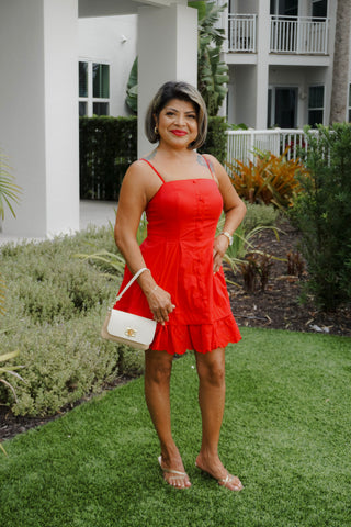 Woman in a red dress standing outdoors with a white building and greenery in the background