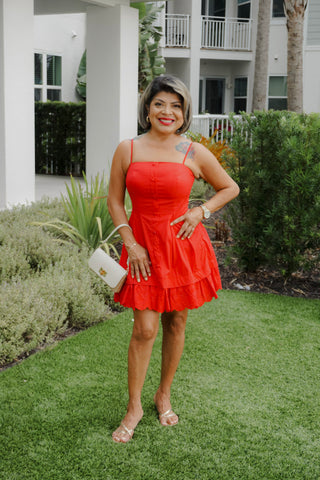 Woman in a red dress standing on grass with a building and trees in the background