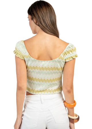 Woman wearing a yellow and white patterned top with white shorts on a plain background