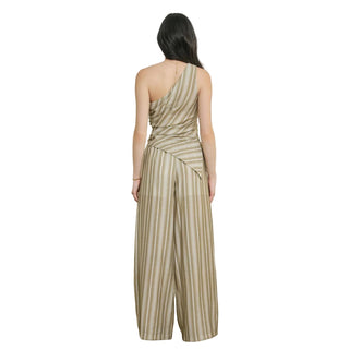 A woman viewed from the back wearing a one-shoulder draped jumpsuit with vertical stripes in beige and olive green, set against a neutral textured wall.