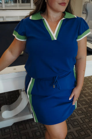 Woman wearing a blue dress with green and white trim in an indoor setting