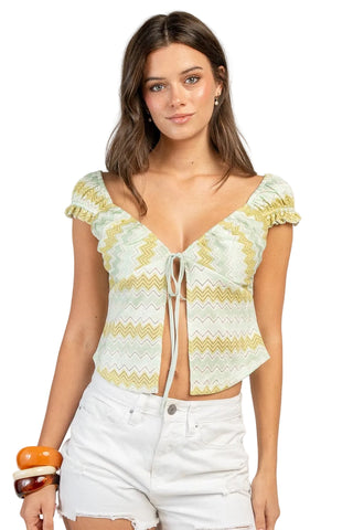 Woman wearing a light green and yellow patterned top with white shorts on a plain background
