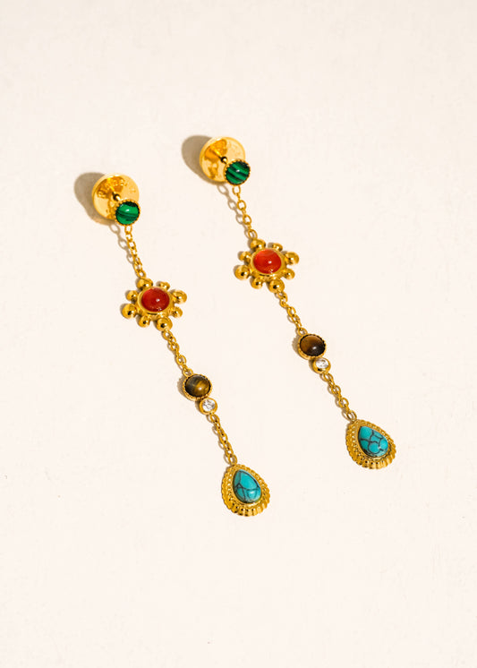 Gold earrings with colorful gemstones on a beige background
