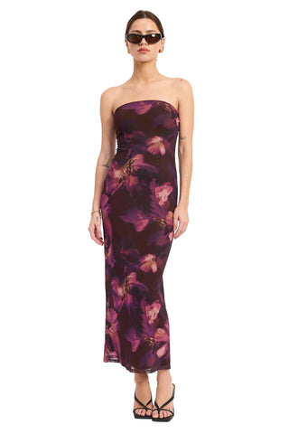 A woman modeling a strapless dark purple maxi dress with a pink and purple floral print, styled with black strappy heels and sunglasses against a plain white studio background.