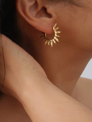 A close-up of a person wearing a small gold crescent moon earring with leaf-like points, shown against skin and dark hair.
