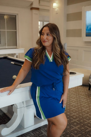 Woman in a blue dress standing next to a pool table in a room with striped walls.