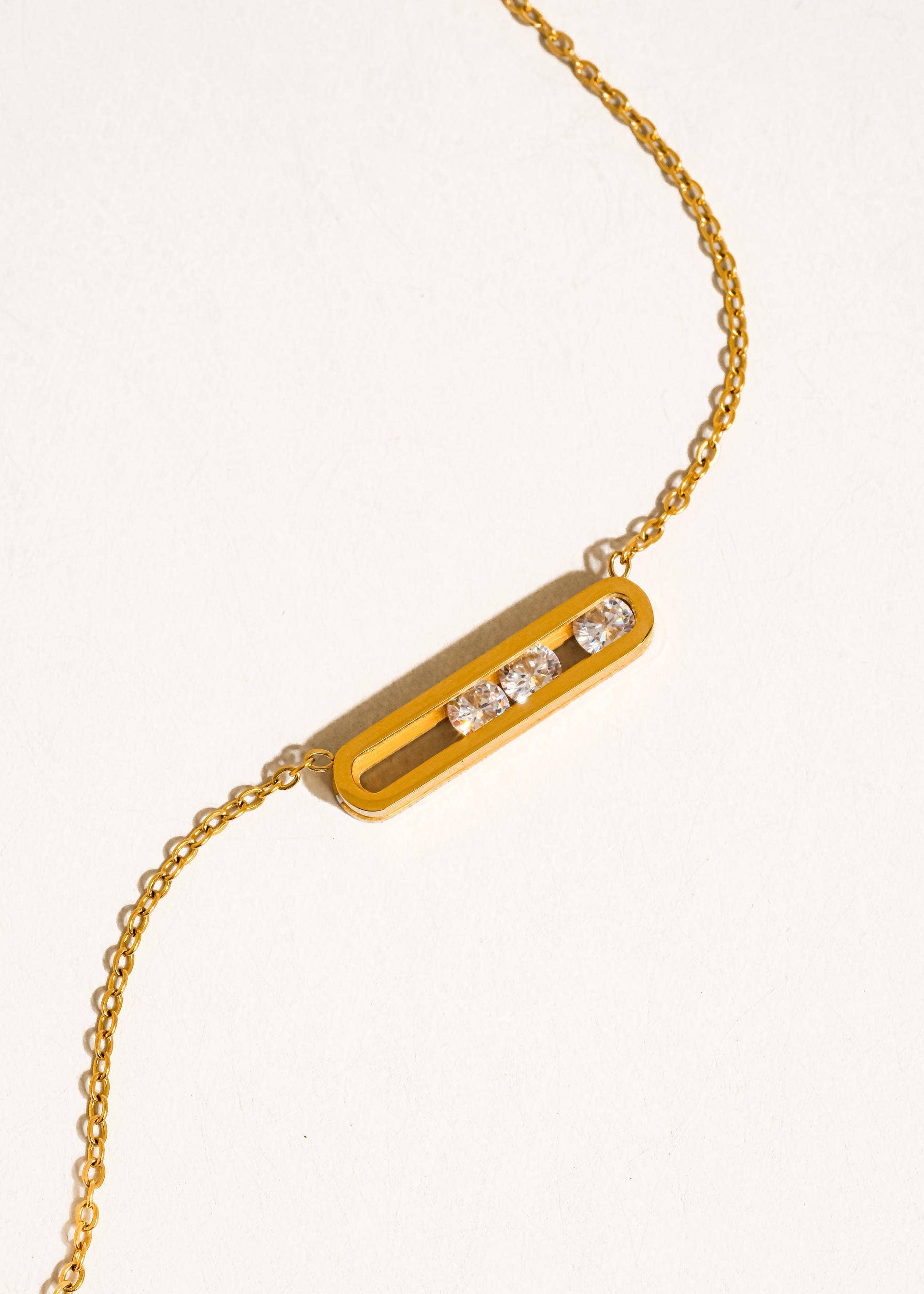 Gold bracelet with a bar-shaped clasp featuring two clear stones on a light beige background