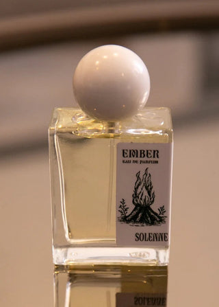 Perfume bottle with a white cap on a reflective surface, blurred background
