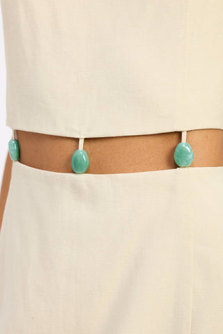 Person wearing a beige outfit with a belt featuring green oval-shaped buttons.