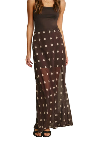 Woman wearing a brown dress with white polka dots against a plain background