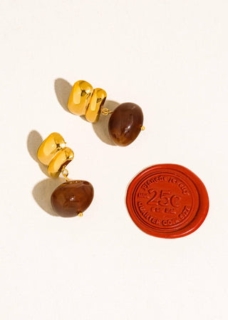 Pair of earrings with gold and brown stones next to a red stamp on a white background
