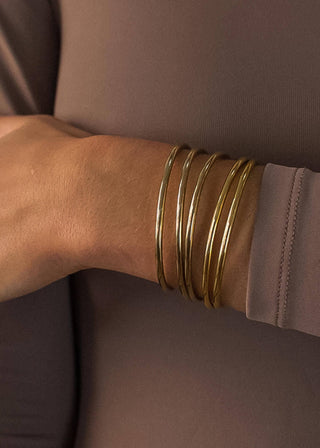 Gold bracelets on a wrist with a neutral background