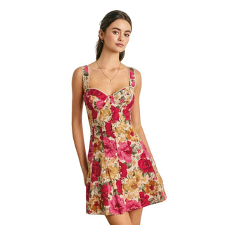 A woman modeling a sleeveless floral mini dress with a sweetheart neckline and wide shoulder straps, set against a light gray paneled wall.