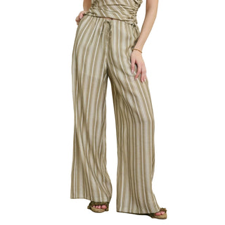 A person wearing high-waisted, wide-leg pants with vertical beige and brown stripes, paired with a matching top and flat sandals, standing against a neutral beige wall.