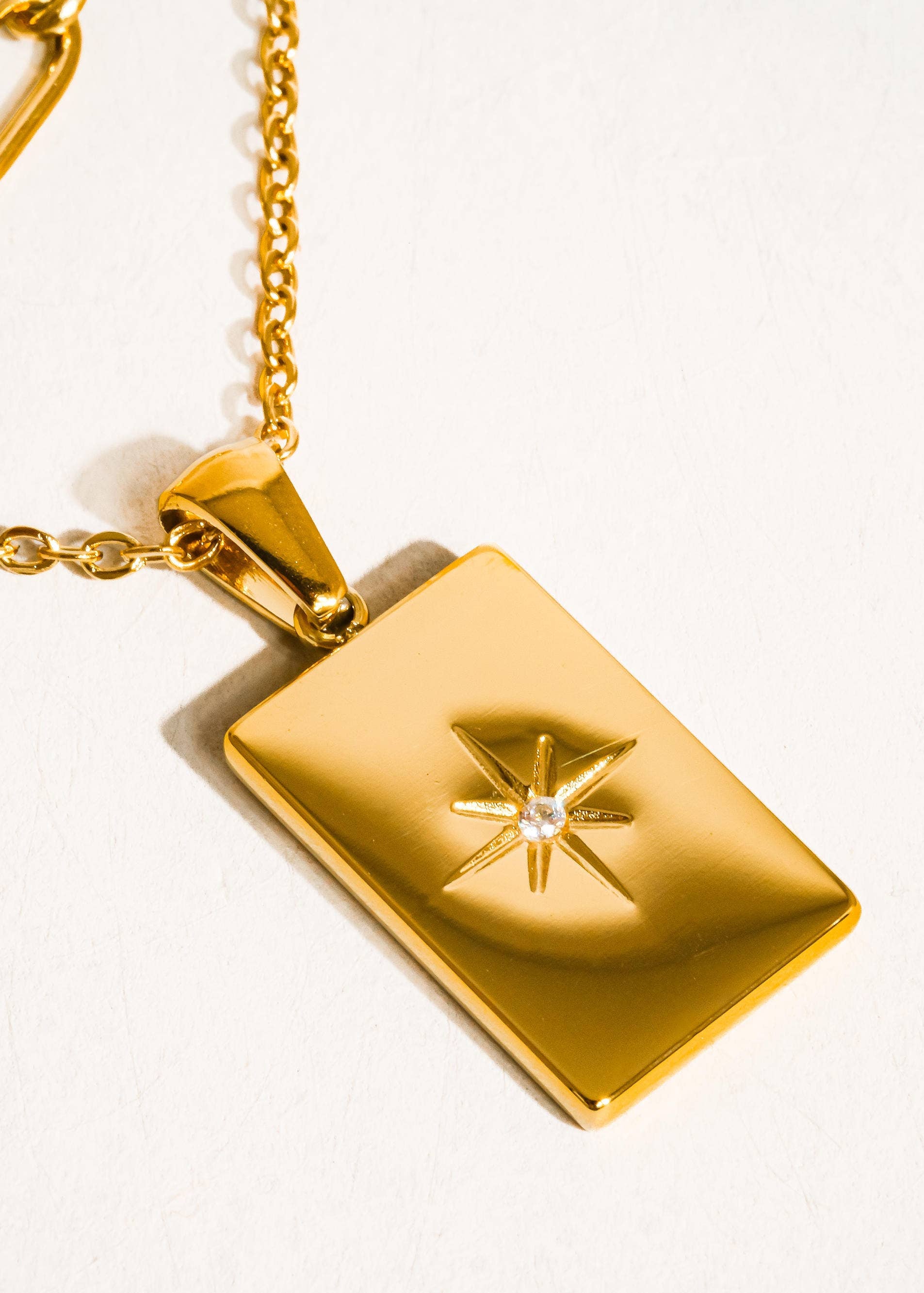 Gold necklace with a rectangular pendant featuring a star design on a white background