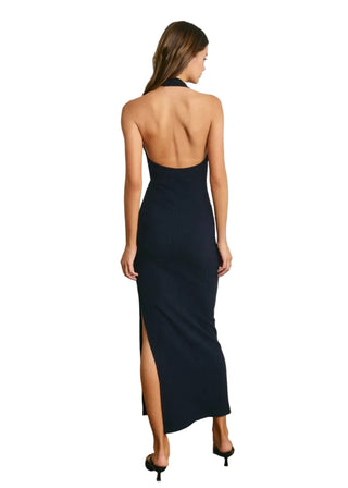Woman wearing a black halter neck dress with a slit, standing against a plain wall.