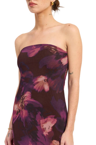 A woman wearing a strapless tube dress with a dark purple and magenta floral print against a plain white background.