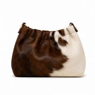 A cowhide shoulder bag with a brown and white mottled pattern, featuring a gathered top and gold-tone hardware, shown on a plain white background.