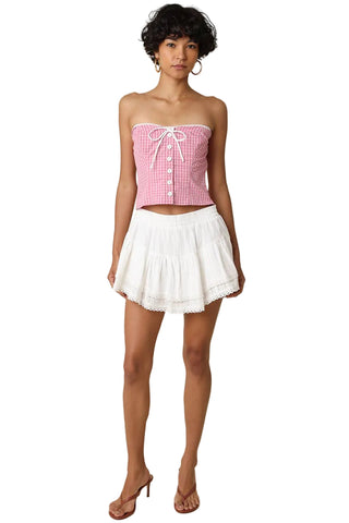 Woman wearing a pink checkered top and white skirt on a beige background