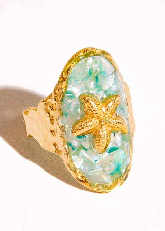 Ring with gold starfish design on a light green stone, set against a white background