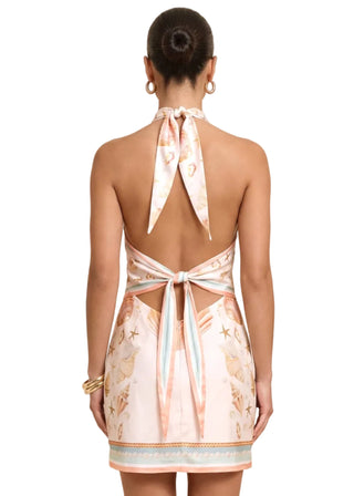 Woman wearing a floral dress with a halter neck and open back on a beige background