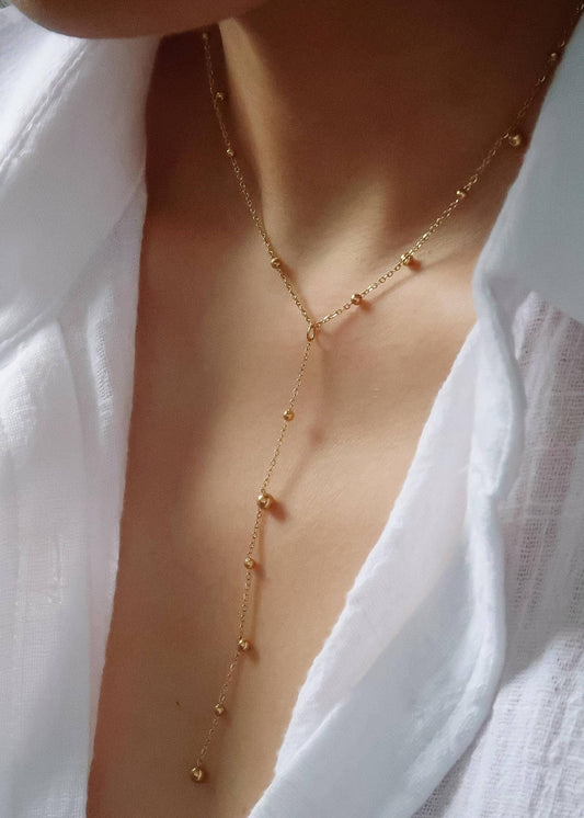 Gold lariat necklace worn by a person with a white shirt