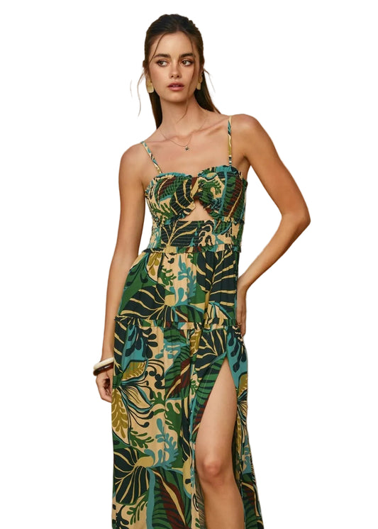 Woman wearing a green and gold tropical floral dress with a slit on a white background