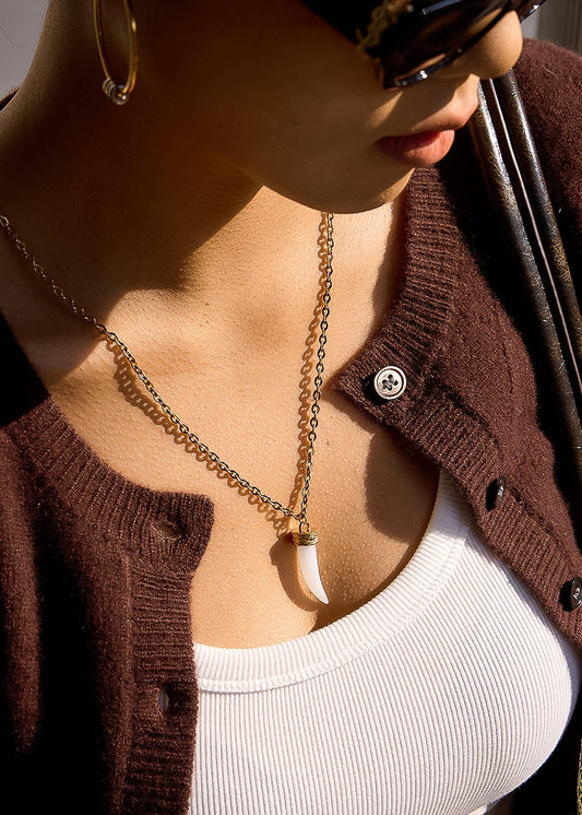 Close-up of a person wearing a brown cardigan and gold necklace.