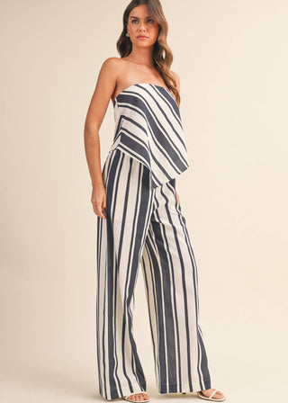 Woman wearing a strapless, navy and white striped jumpsuit on a beige background