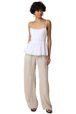 Woman wearing a white top and beige pants against a beige background