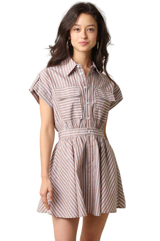 A woman modeling a short-sleeve collared shirt dress with vertical brown and beige stripes, featuring a button-up front, chest pockets, and a matching fabric tie belt at the waist, set against a plain beige background.