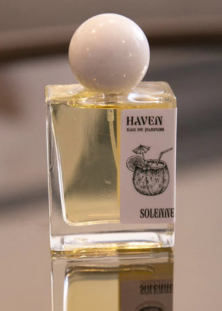 Perfume bottle with a white sphere cap on a reflective surface, featuring the brand 'HAVEN'.