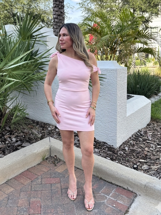 Woman in a pink dress standing outdoors with greenery in the background