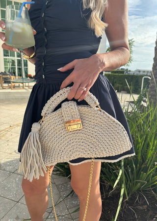 Person holding a woven handbag with a drink in an outdoor setting
