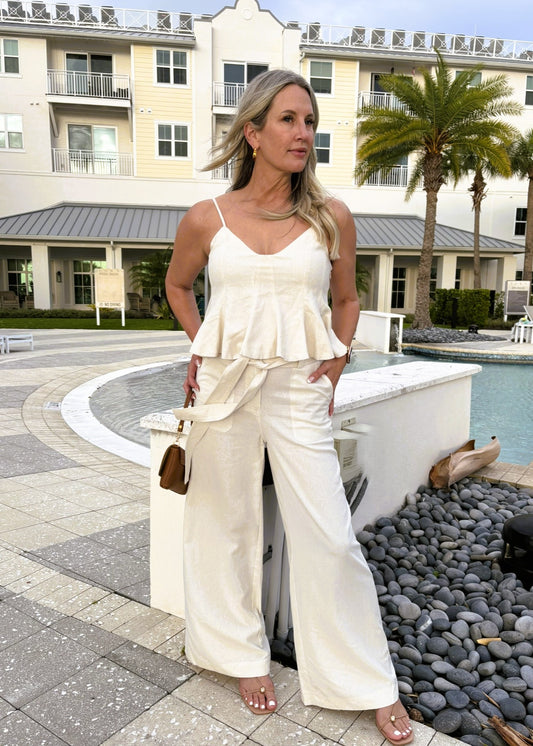 Woman in a white outfit standing by a pool with palm trees in the background