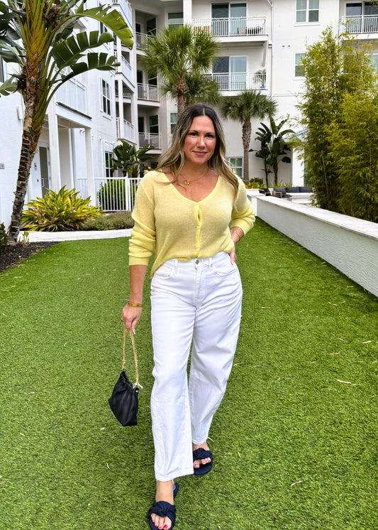 Woman in yellow top and white pants standing on grass with a building in the background