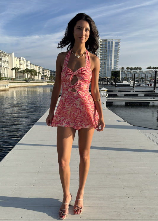 Woman in a pink floral dress standing on a dock with water and buildings in the background