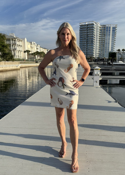 Woman in a strapless dress with animal prints standing on a dock with buildings and water in the background.
