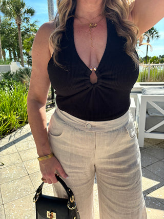 Woman wearing a black top and beige pants outdoors with palm trees in the background