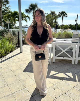 Woman in black top and beige pants standing outdoors with palm trees in the background