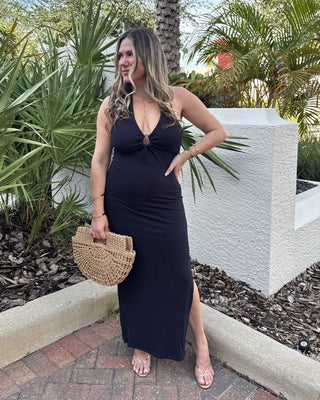 Woman in a navy dress standing outdoors with plants and a white structure in the background