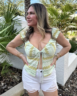 woman in chevron green and blue top with tropical background