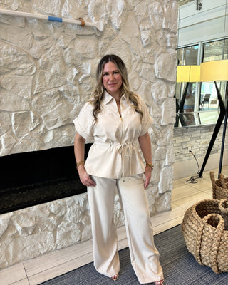 Woman in a white outfit standing in a room with stone walls and decorative elements.