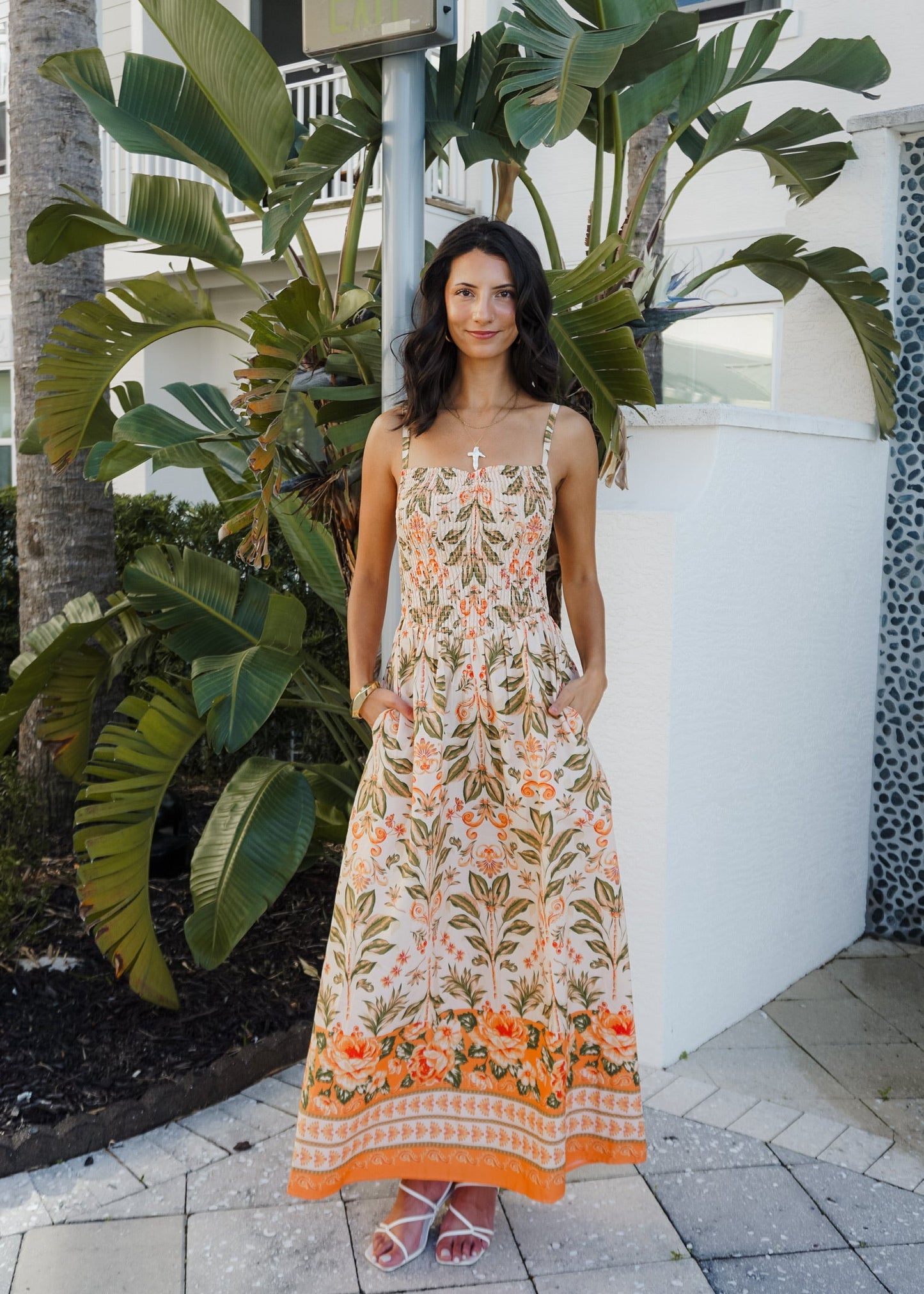Woman in a floral dress standing outdoors with plants and a building in the background