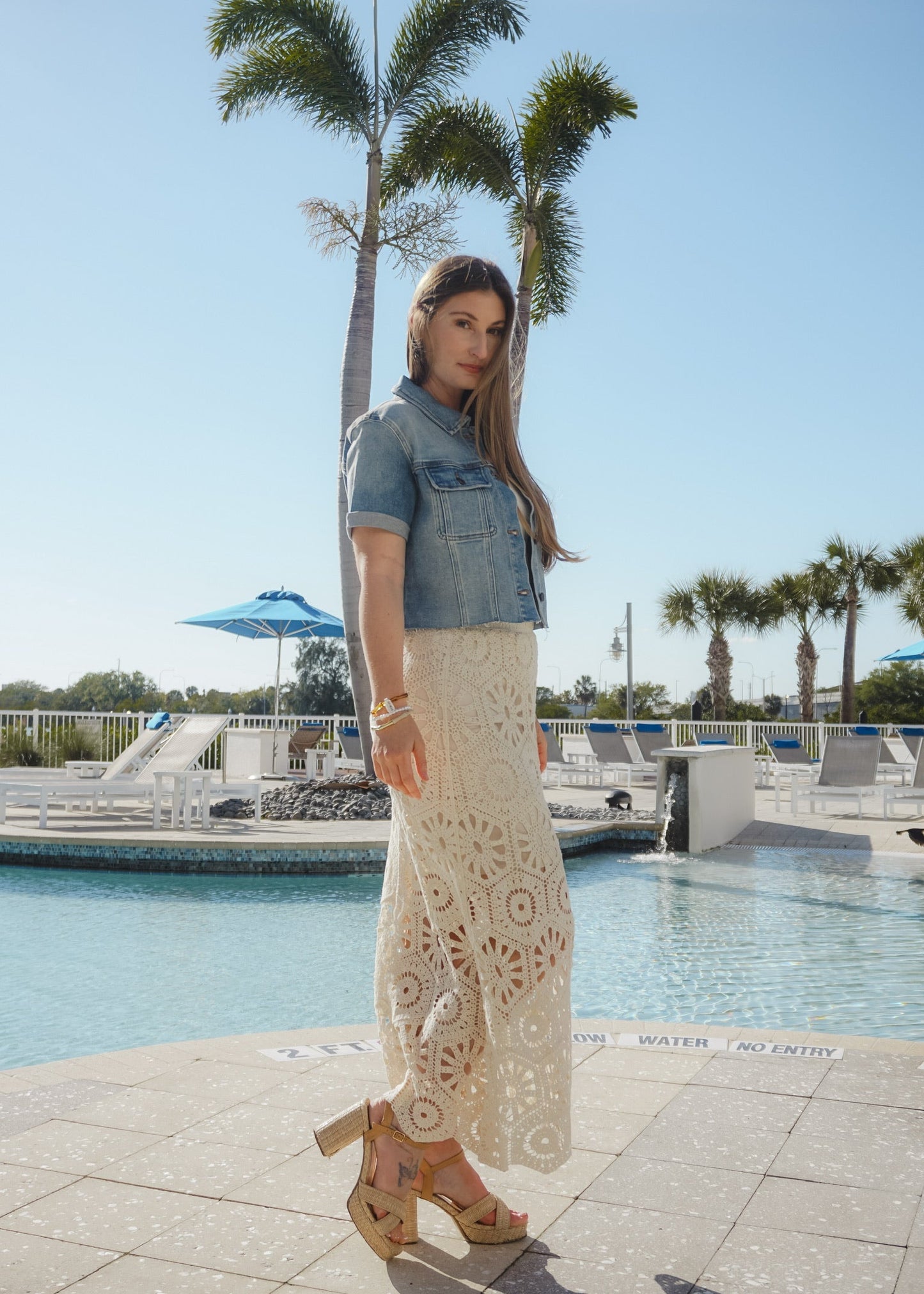 Woman standing by a pool with palm trees in the background
