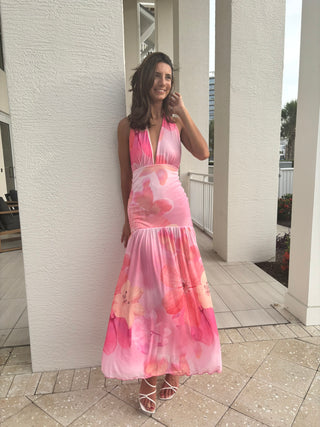 Woman in a pink floral dress standing against a white wall.
