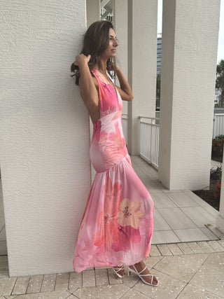 Woman in a pink floral dress standing against a white wall.